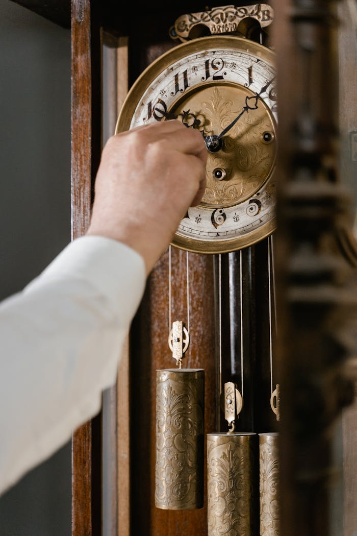 An aged hand adjusting an intricate antique wall clock, capturing a moment of nostalgia.